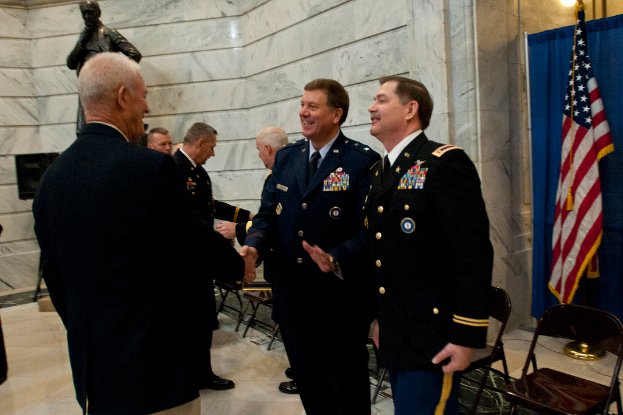 Menschen schütteln sich die Hände vor Stühlen, mit einer Statue, einer Flagge und einem Vorhang im Hintergrund.