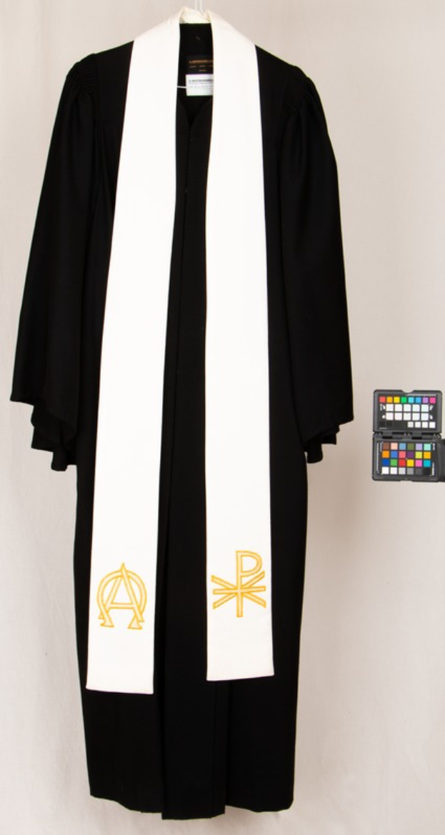 Ein schwarzer Umhang mit einem weißen Schalk darüber hing an einem Bügel vor einem weißen Hintergrund, daneben ein weiterer Schalk.