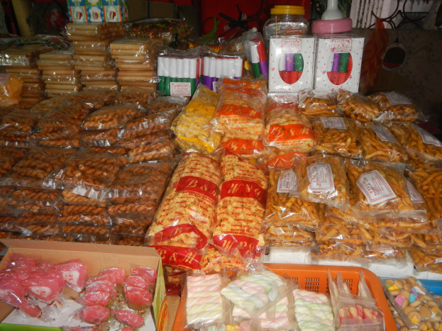 Ein Marktstand mit verschiedenen Lebensmittelverpackungen, Flaschen und Schachteln, mit einem Tisch voller verschiedener Lebensmittel im Vordergrund und einer Wand im Hintergrund.