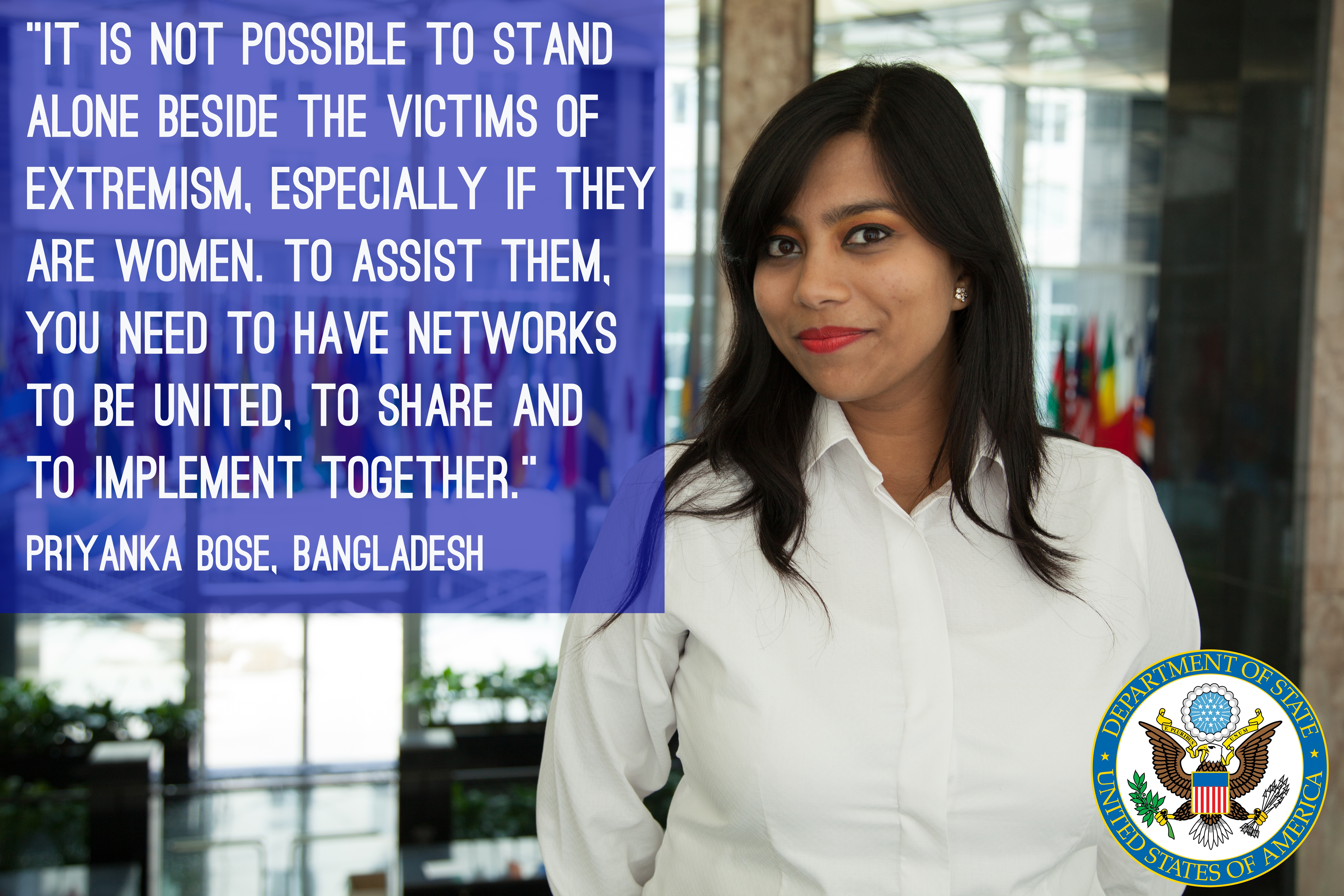 Eine Frau in einem weißen Hemd steht vor einem Gebäude mit einem Zitat über Einheit und Unterstützung für Opfer von Extremismus, insbesondere Frauen, mit einem Logo in der rechten unteren Ecke.