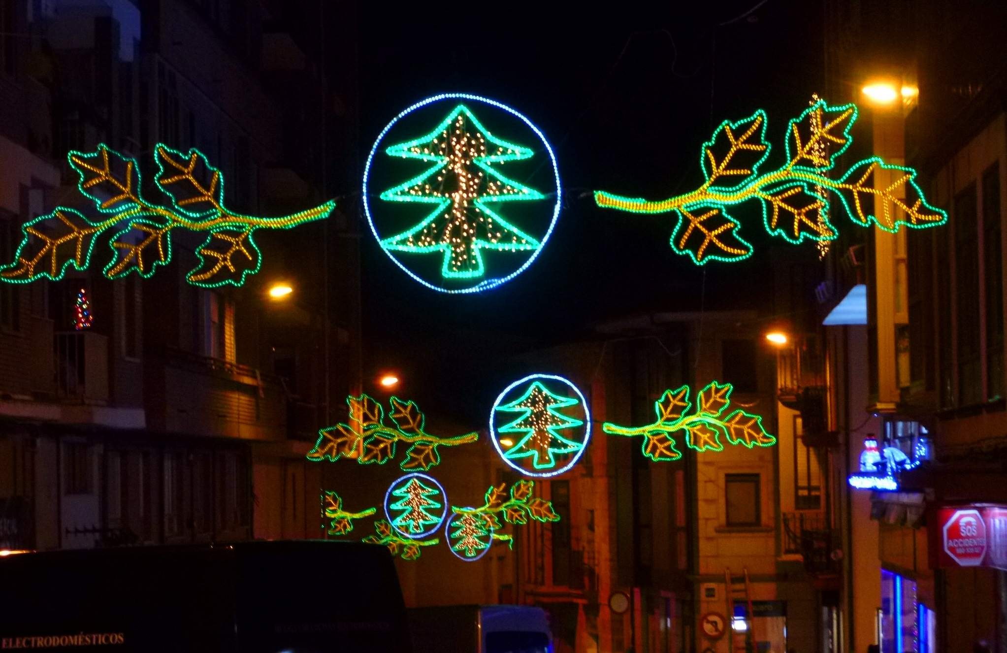 Festliche Weihnachtsbeleuchtung mit Blattdekoration erhellt eine Stadtstraße, an der Fahrzeuge an Gebäuden auf beiden Seiten vorbeifahren.