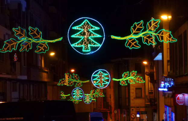 Festliche Weihnachtsbeleuchtung mit Blattdekoration erhellt eine Stadtstraße, an der Fahrzeuge an Gebäuden auf beiden Seiten vorbeifahren.