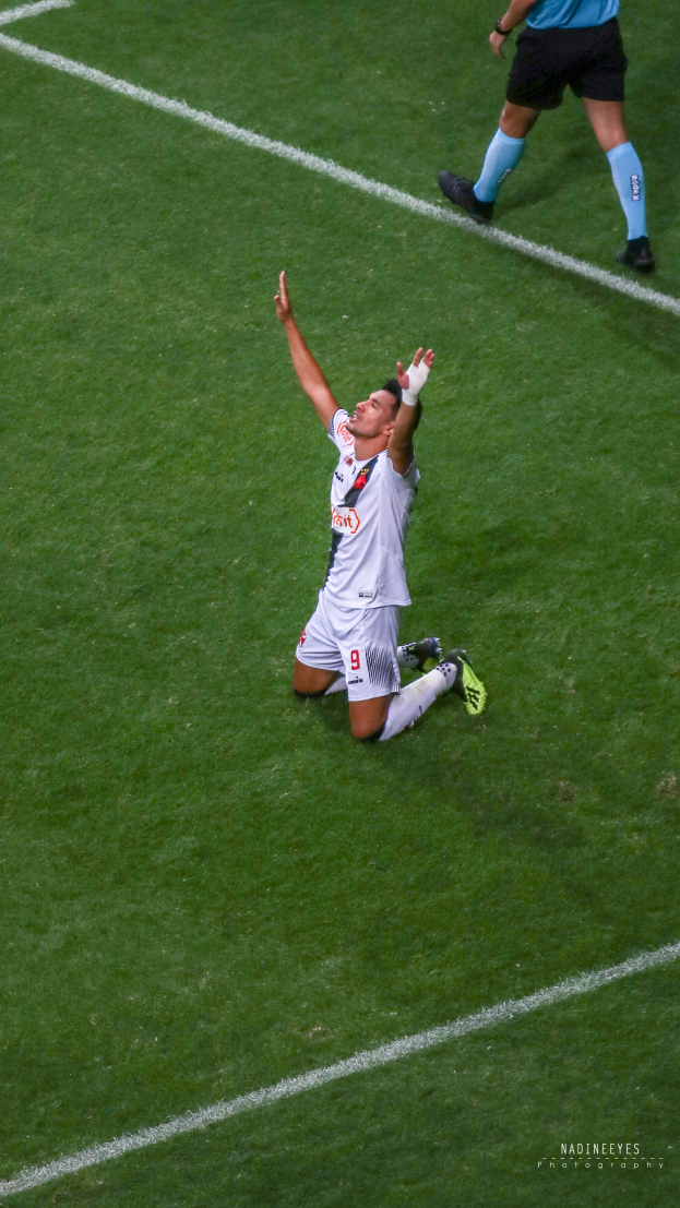Ein Fußballspieler kniet auf dem Boden und feiert mit ausgestreckten Armen, trägt eine Sportuniform und Schuhe.