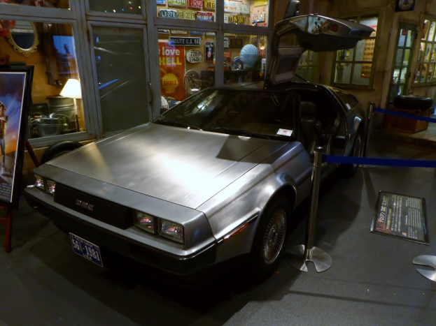 Ein DeLorean DMC-12 aus der Zurück in die Zukunft-Reihe wird in einem Museum ausgestellt, umgeben von Informationsanzeigen, Bändern und verschiedenen Gegenständen.