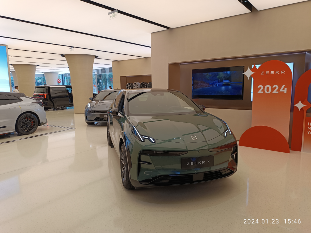 Eine Autohalle mit Ausstellungsfahrzeugen, Informationsschildern, einem wandmontierten Fernseher, Deckenleuchten und einem Wasserzeichen, das Teil von Zeekrs neuer Autohalle ist.