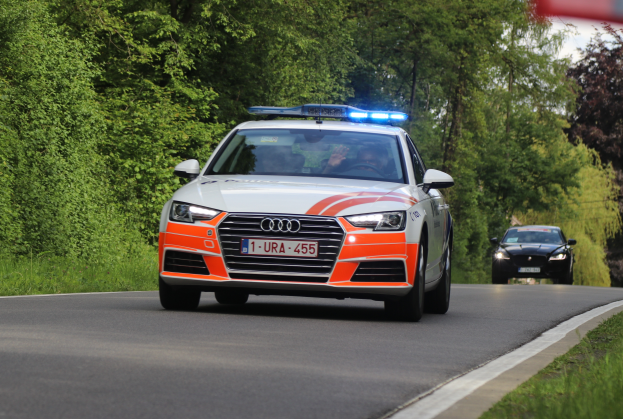 Ein Audi A4 Polizeiwagen fährt auf einer grasbewachsenen Straße neben einem Wald, mit zwei Personen drinnen, unter einem klaren blauen Himmel.
