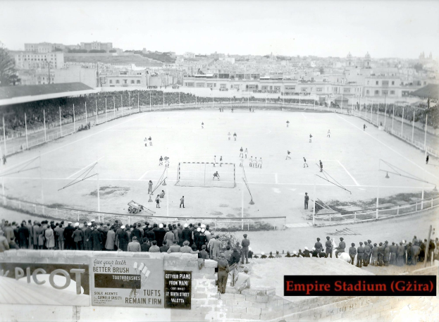 Ein altes Schwarz-Weiß-Foto des Empire Stadiums in Giza mit einer Gruppe von Menschen, die in der Mitte Eis hockey spielen, umgeben von einem Zaun, Gebäuden und Bäumen im Hintergrund und Text unten.