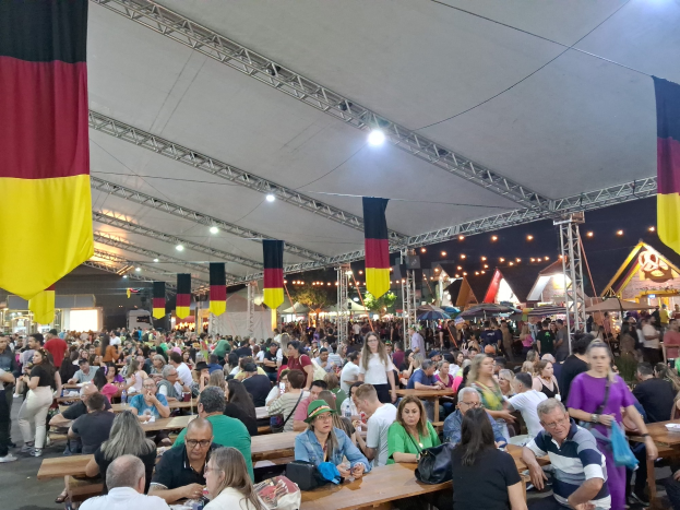 Eine große Gruppe von Menschen sitzt an Tischen unter einem Zelt auf dem Oktoberfest in München, Deutschland, mit Taschen und Gegenständen auf den Tischen, umgeben von festlichen Décors und anderen Zelten.