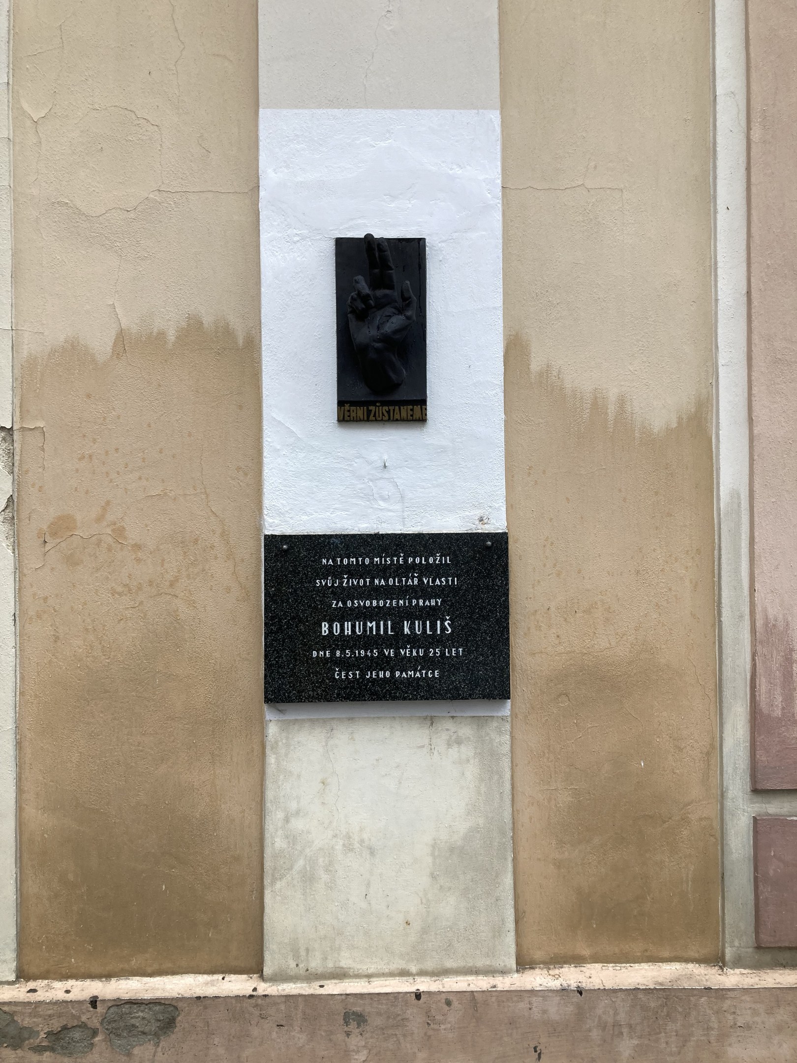 Schwarze Plakette an einem Gebäude mit einer Hand darauf, beschriftet mit Text, wahrscheinlich ein Holocaust-Denkmal.
