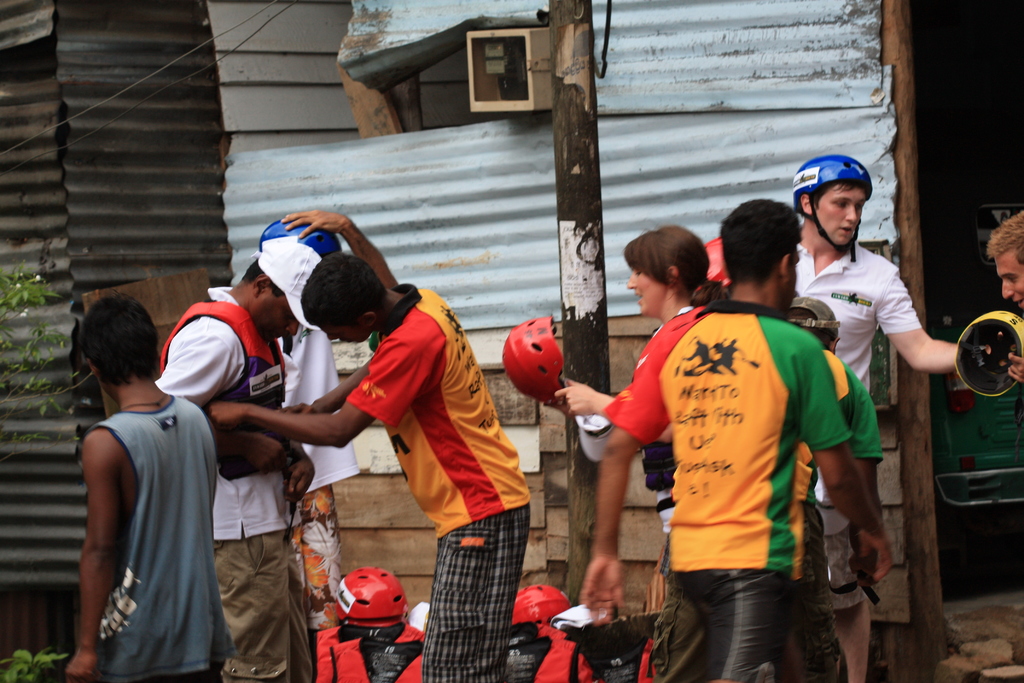 Eine Gruppe von Menschen vor Dachplatten mit roten Helmen auf dem Boden und einem Pfahl daneben.