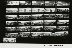 Ein Schwarz-Weiß-Foto einer vielseitigen Menschenmenge, die um einen Fernseher versammelt ist und strahlt, mit Text unten.