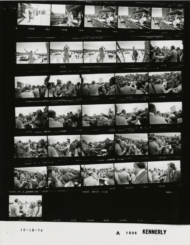 Ein Schwarz-Weiß-Foto einer vielseitigen Menschenmenge, die um einen Fernseher versammelt ist und strahlt, mit Text unten.