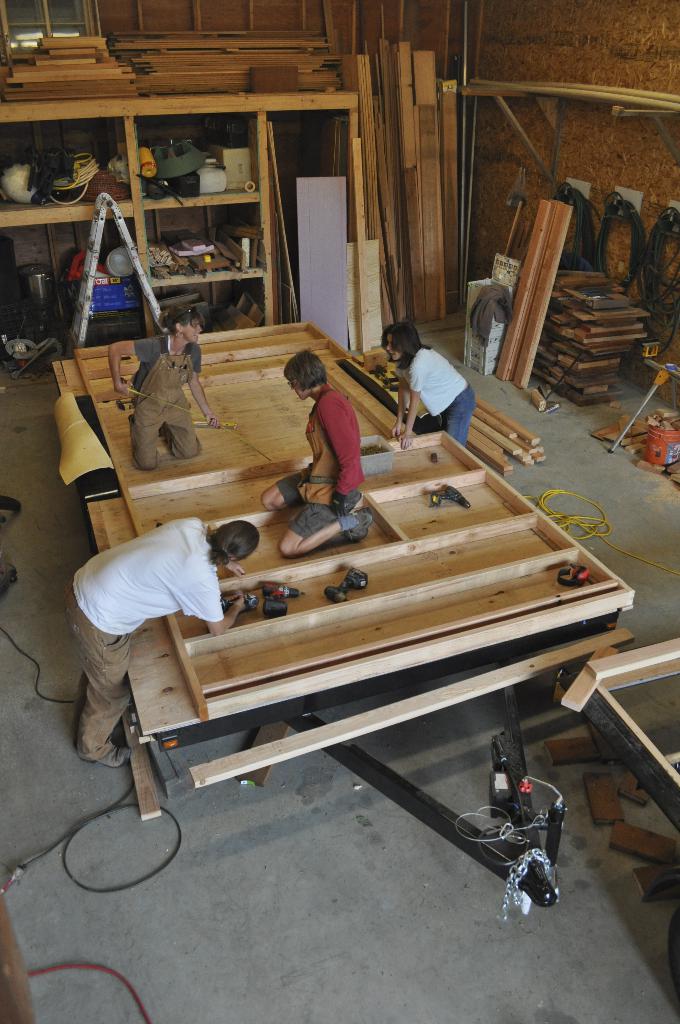 Eine Schreinerwerkstatt mit mehreren Menschen bei der Arbeit mit verschiedenen Werkzeugen und Geräten.