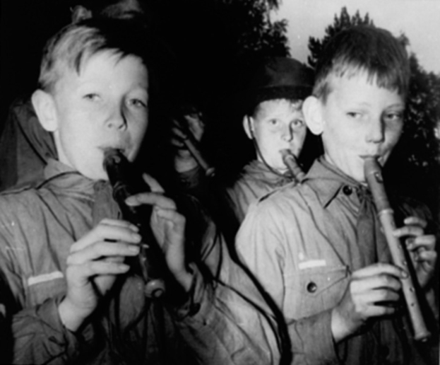 Eine Gruppe junger Jungs, die Flöten im Freien spielen mit Bäumen im Hintergrund.