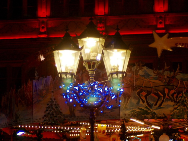 Eine Straßenlaterne mit dekorativen Lichtern und Ornamenten steht in einer Stadt in der Nacht, mit einem Gebäude im Hintergrund.