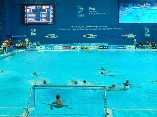 Wasserballspieler bei einem Poolwettkampf während der FINA-Weltmeisterschaften 2016 in Kazan, mit Zuschauern auf der linken Seite und einem Werbeplakat im Hintergrund.