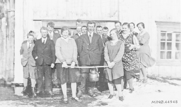 Eine Gruppe strahlender Menschen in Schwarz und Weiß, die ein Band vor einem Gebäude mit einem Fenster und einer Tür halten, feiern die Eröffnung einer neuen Schule.