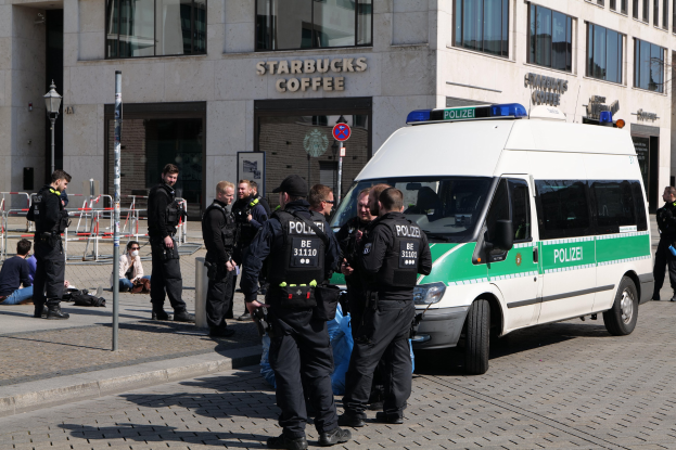 Eine Gruppe von Polizisten steht vor einem Starbucks-Café mit einem Van auf der rechten Seite und einigen Menschen auf der linken Seite; ein Gebäude, ein Schild, ein Lichtmast und ein Zaun sind im Hintergrund zu sehen.