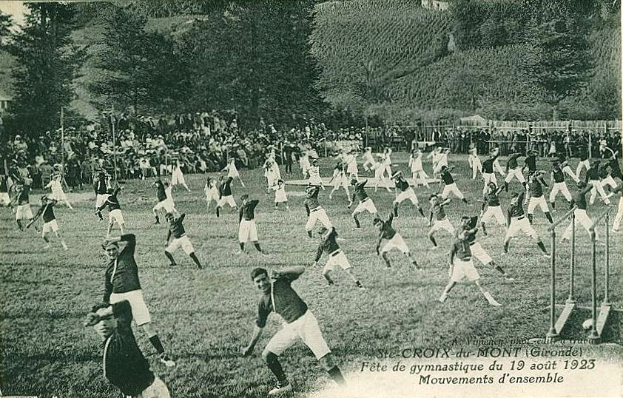 Ein Schwarz-Weiß-Foto einer Gruppe, die auf einem Rasenfeld Fußball spielt, mit Bäumen und Gebäuden im Hintergrund, datiert auf den 19. August 1923.