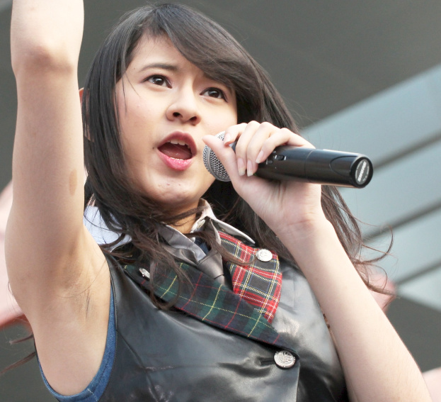 Frau singt leidenschaftlich in ein Mikrofon auf der Bühne, trägt ein weißes Hemd und einen Pferdeschwanz, hat die Augen geschlossen und einen konzentrierten Gesichtsausdruck.