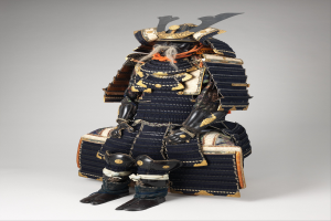 Ein japanischer Samurai in voller Rüstung, einschließlich Helm und Schwert, steht vor einem weißen Hintergrund. Die Rüstung ist kunstvoll gestaltet und das Schwert fest in der Mitte gehalten.