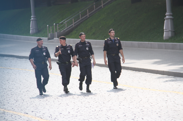 Drei Polizisten in Uniform, die eine Straße entlanggehen mit Pfählen, Geländern, Treppen und Gras im Hintergrund.