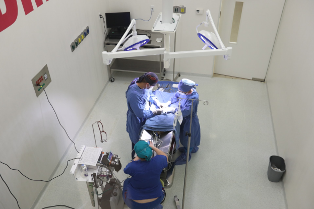 Chirurgen führen einen Eingriff an einem Patienten in einem Operationssaal mit medizinischer Ausrüstung, einer Wand mit Text und einem Objekt auf dem Boden durch.