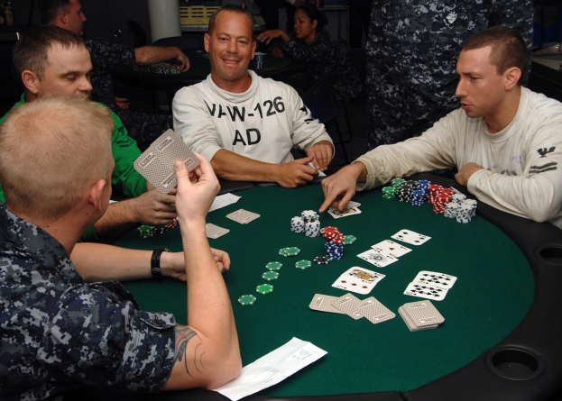 Eine Gruppe von Männern sitzt um einen Tisch und spielt Poker, mit Münzen und Karten vor ihnen ausgebreitet während eines Turniers.