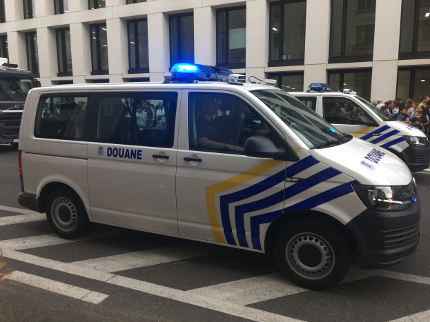 Eine Gruppe von Douane-Polizeiwagen auf einer Stadtstraße geparkt, mit Menschen im Inneren und einem beleuchteten Gebäude im Hintergrund.