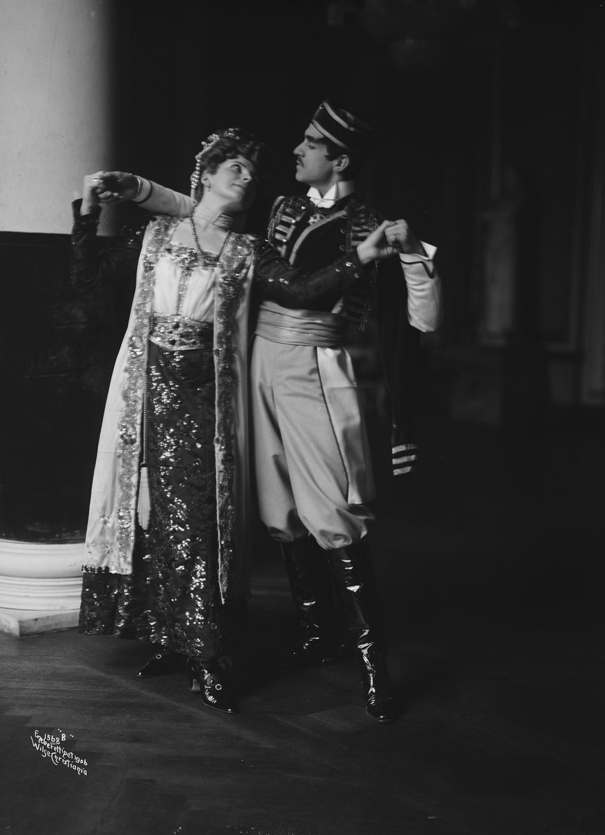 Schwarzes und weißes Foto eines Mannes und einer Frau, die in einem Ballsaal tanzen, mit einer Säule und einer Wand im Hintergrund; der Mann trägt Schuhe.