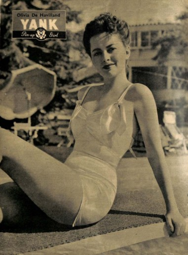 Olivia de Havilland in einem Bikini sitzend auf dem Boden und lachend, mit Bäumen, Stühlen, einem Gebäude und Text im Hintergrund.