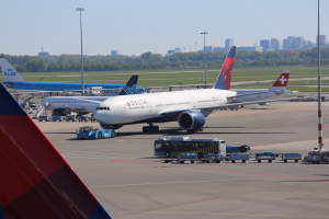 Ein Boeing 777-300ER der Delta Air Lines steht auf dem Frankfurt Airport, umgeben von Fahrzeugen und Laternenmasten, sowie Gebäuden, Bäumen und einem klaren blauen Himmel.