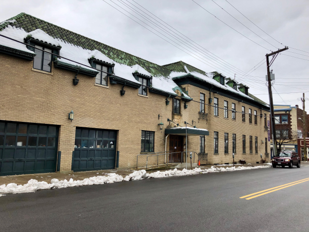 Großes Backsteingebäude mit einem grünen Dach an einer Straßenkreuzung, beschriftet als ehemalige Feuerwache St. Louis, umgeben von Fahrzeugen, Schnee, Strommasten, Bäumen und einem bewölkten Himmel.
